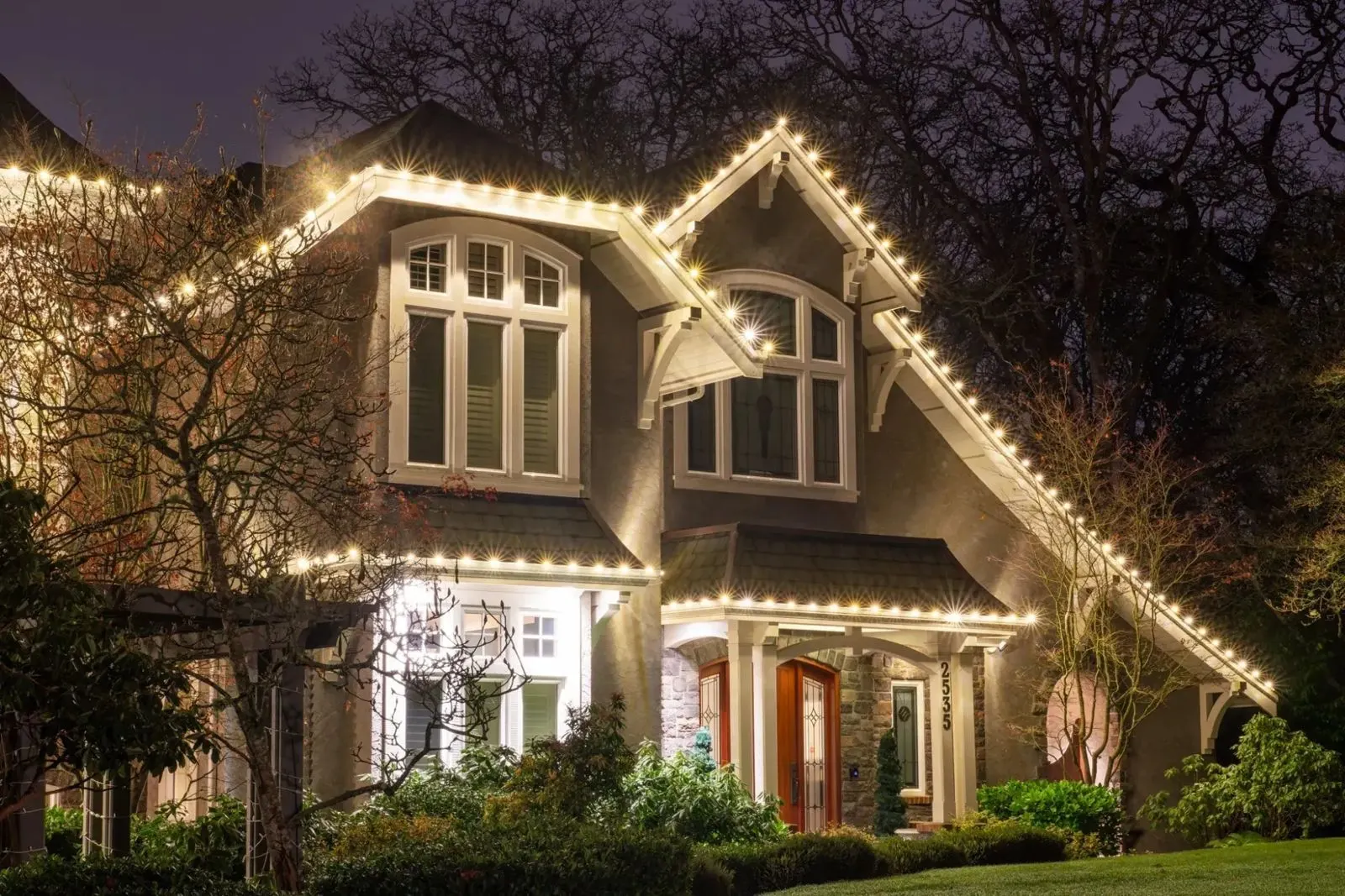 A two-storey home at dusk with warm white lights along every roofline